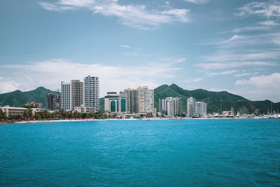 Sea by city buildings against sky