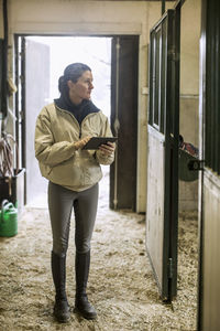 Full length of mid adult woman using digital tablet in horse stable