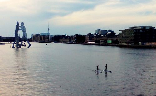 Silhouette people on sea by city against sky