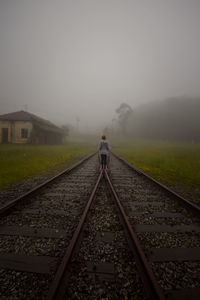 Rear view of man standing on railroad track against sky
