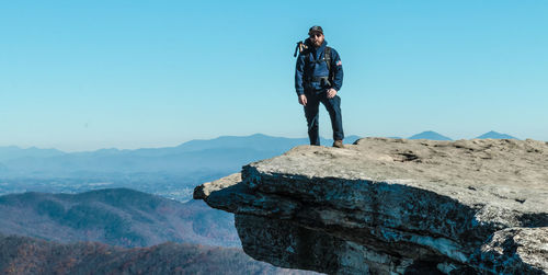 Man standing on rock against blue sky