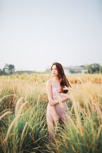 Young woman standing on grassy land against clear sky