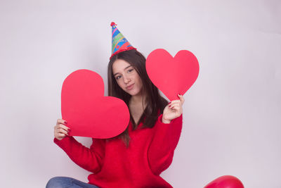 Midsection of woman holding heart shaped balloons against gray background