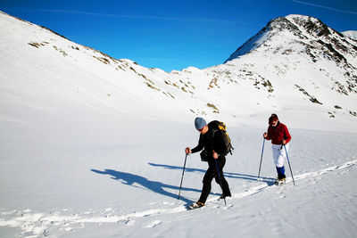 Rear view of people skiing on snowcapped mountain against sky