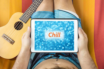 Midsection of man using digital tablet while sitting on bed by guitar at home