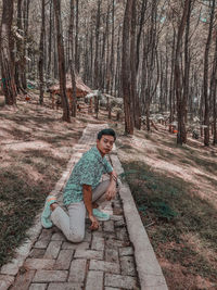 Portrait of boy sitting on tree trunk in forest