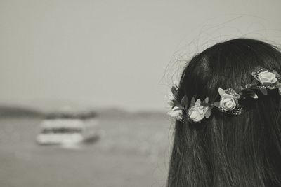 Rear view of woman wearing wreath by sea against sky