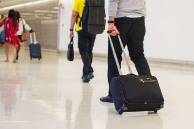 Rear view of people with luggage walking on tiled floor at airport