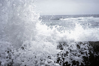 Waves splashing on shore against sky