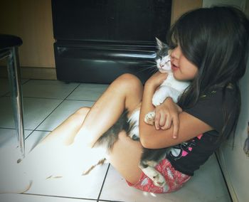 Cute girl embracing cat while sitting on floor at home
