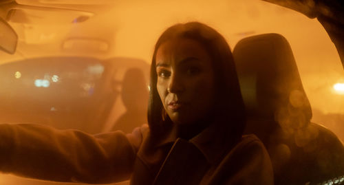 Portrait of serious woman enjoying night drive while sitting in car and looking at the camera