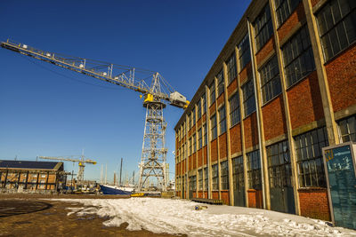 Low angle view of crane by building against clear sky