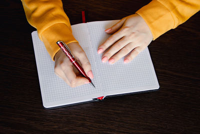 Cropped hands of woman writing in book on table