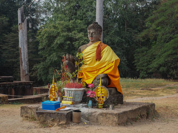 Statue of man sitting by tree trunk in forest