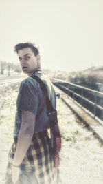 Portrait of young man standing on railing against sky