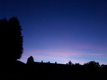 Silhouette trees on field against clear blue sky during sunset