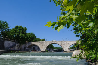 Arch bridge over river against clear blue sky