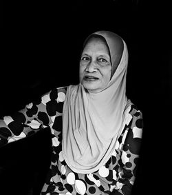 Portrait of woman in hijab sitting against black background