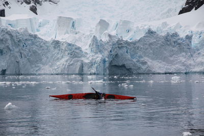 Person practicing rolling kayak in river against glacier