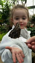 Cute girl looking at butterfly held by woman