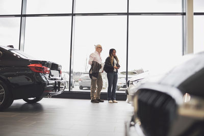 Man and woman with paper standing by glass window at car showroom