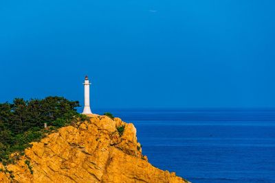 Lighthouse by sea against clear blue sky