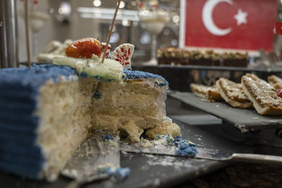 Half eaten layered cake with blue whipped cream on table in buffet