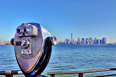 Binoculars at railing by sea against sky