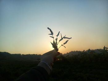 Midsection of man holding umbrella against sky during sunset