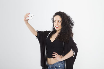 Portrait of smiling young woman photographing against white background