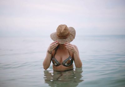 Sensuous woman wearing bikini holding sun hat while standing in lake