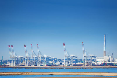 Cranes at harbor against clear sky