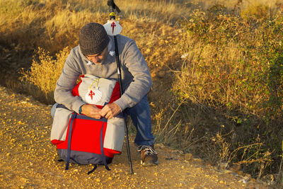 Male hiker with backpack crouching on field