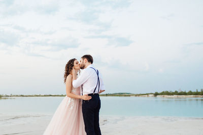 Rear view of couple standing by water against sky