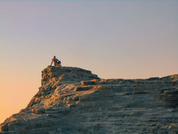 Rear view of man standing on a rock against the clear sky at the sunset