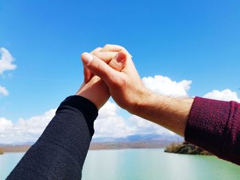Cropped hands of couple over lake against sky