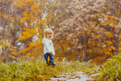 Full length portrait of boy standing on plants during autumn