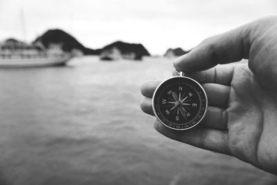 Cropped hand holding navigational compass against sea