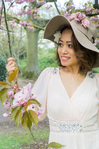 Young woman wearing hat standing against pink flowers