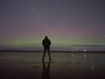 Rear view of man standing on beach against sky at night
