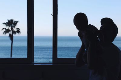 Silhouette couple standing by sea against sky