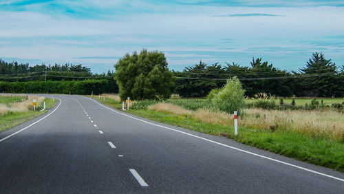 Road by trees on landscape against sky