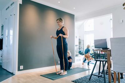 Woman exercising with resistance band by girls in living room