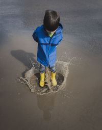 High angle view of playful boy wearing rubber boots while jumping in puddle