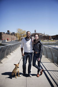 Portrait of happy couple with dog on footbridge against clear sky