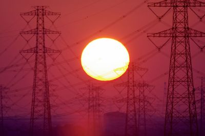 Low angle view of electricity pylon against sky during sunset