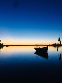 Silhouette boat moored in lake against clear blue sky during sunset