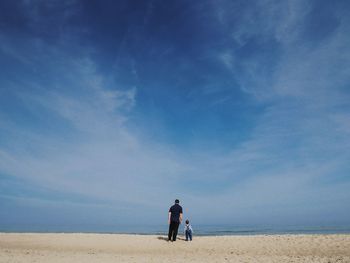 Rear view father and son at beach against sky