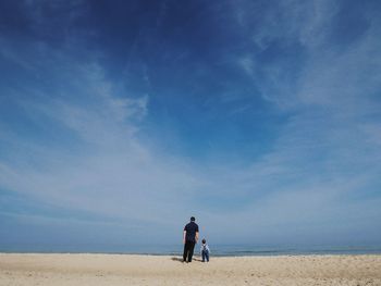 Rear view father and son at beach against sky