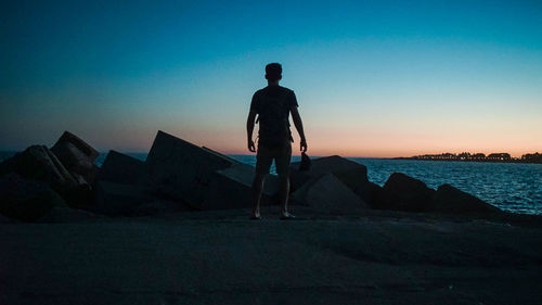 Silhouette man standing on rock by sea against clear sky